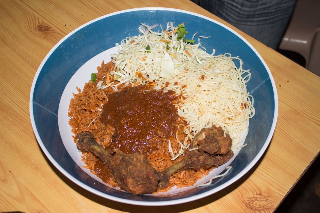 A bowl of Ghanaian-style jollof rice with chicken, pepper sauce and shredded cabbage