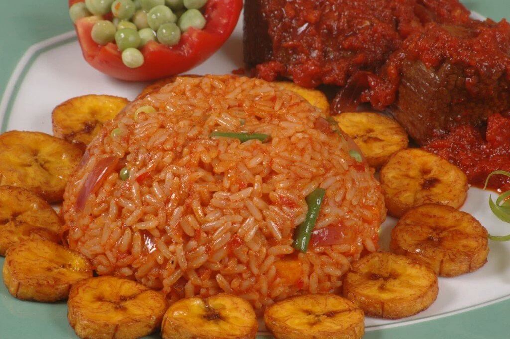 A plate of red-orange jollof rice served with fried plantain slices