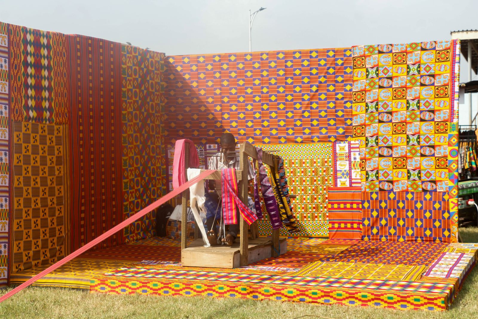 Kente weavers at work on narrow-strip looms in Ghana, with long warp threads stretched out in front